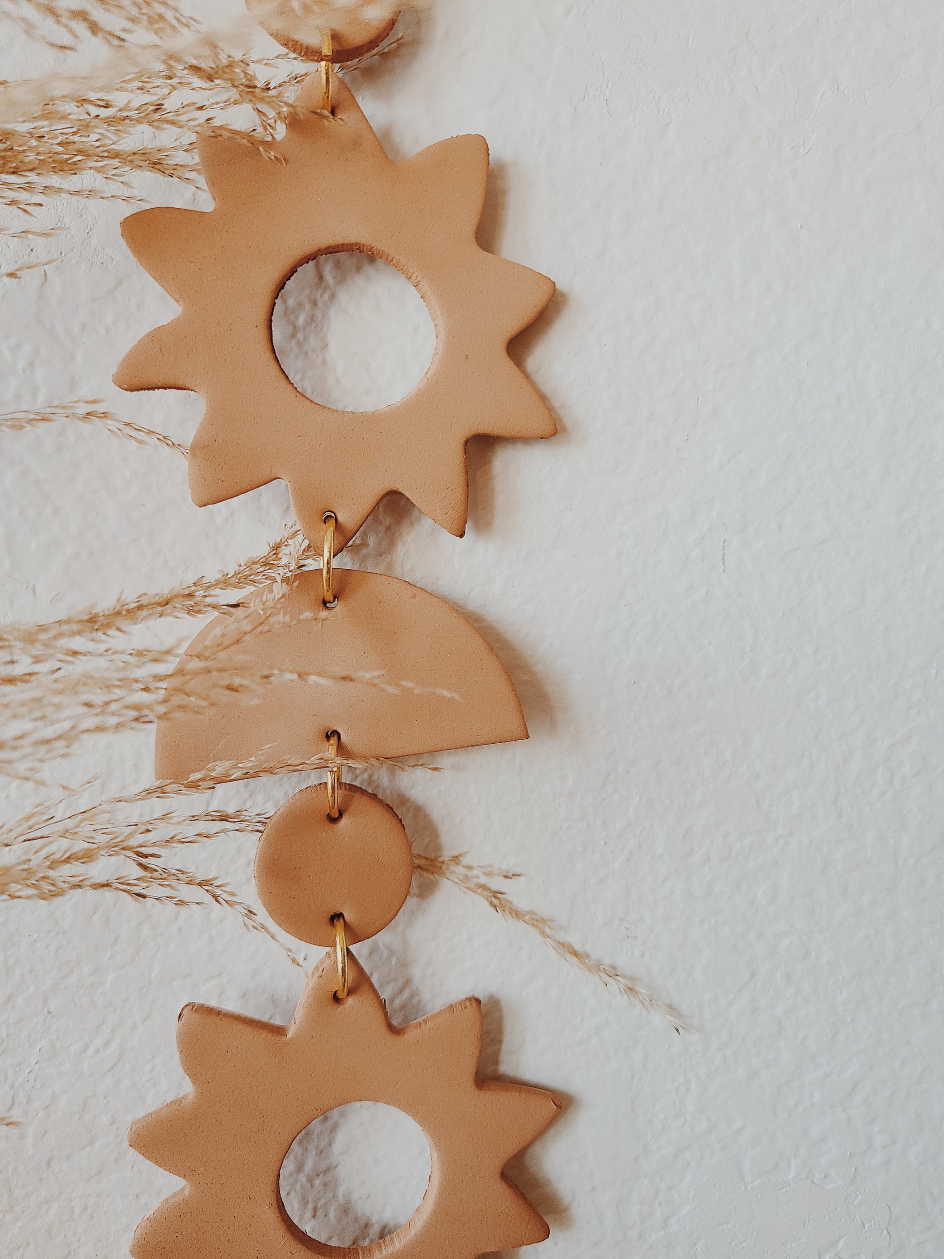 a close up of the sun wall hanging we have a rust terracotta colored clay with gold jump rings to exude warmth. 