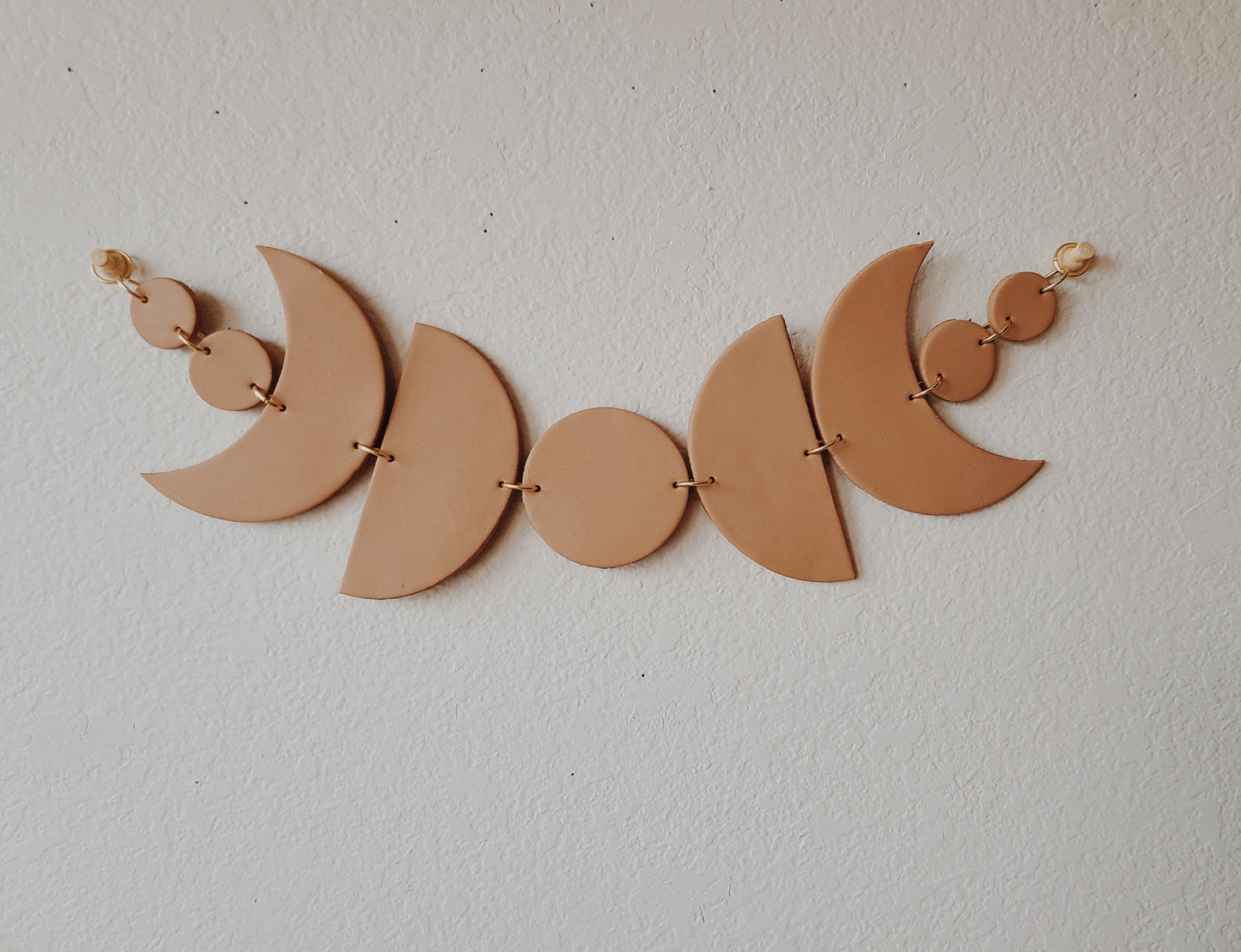 Create a lunar look to liven up your living space with this Clay Crafted Moon Phase terracotta design. Handmade for unique styling, this eye-catching piece promises to always add a touch of charm to your interior. front side hanging horizontally